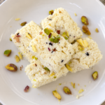Homemade kalakand topped with pistachios on a white plate