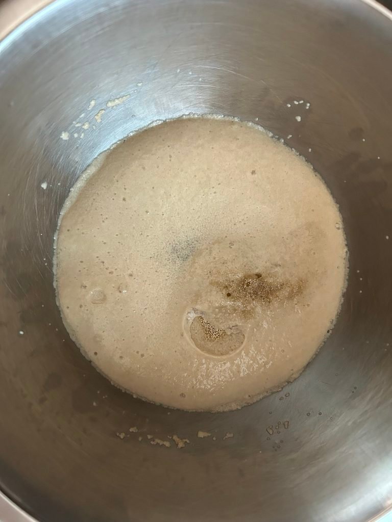 Active dry yeast mixed with warm water and sugar, forming bubbles and foam in a mixing bowl.
