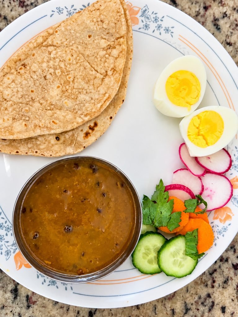 Homemade meal with dal, roti, boiled egg, and fresh vegetable salad served on one plate.