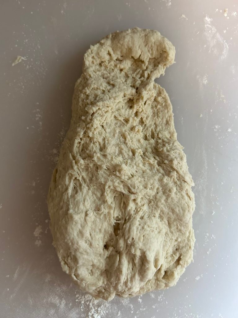 Rough and sticky homemade bread dough on a flat surface before kneading.